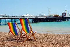 View of Brighton pier from the beach with two rainbow deck chairs in the foreground