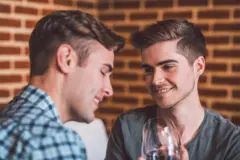 Two happy gay men on a date drinking red wine