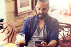 Man sitting in a pub holding his phone texting while drinkg a pint of beer