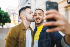 Two happy gay men taking a selfie while one kisses the other