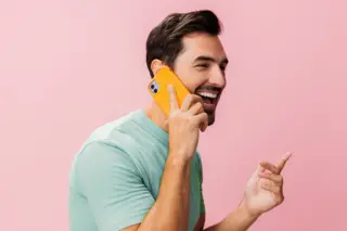 Gay man in front of a pink background talking and laughing on a mobile phone