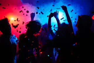 Silhouettes of dancers moving in confetti with with pulsating lights and music